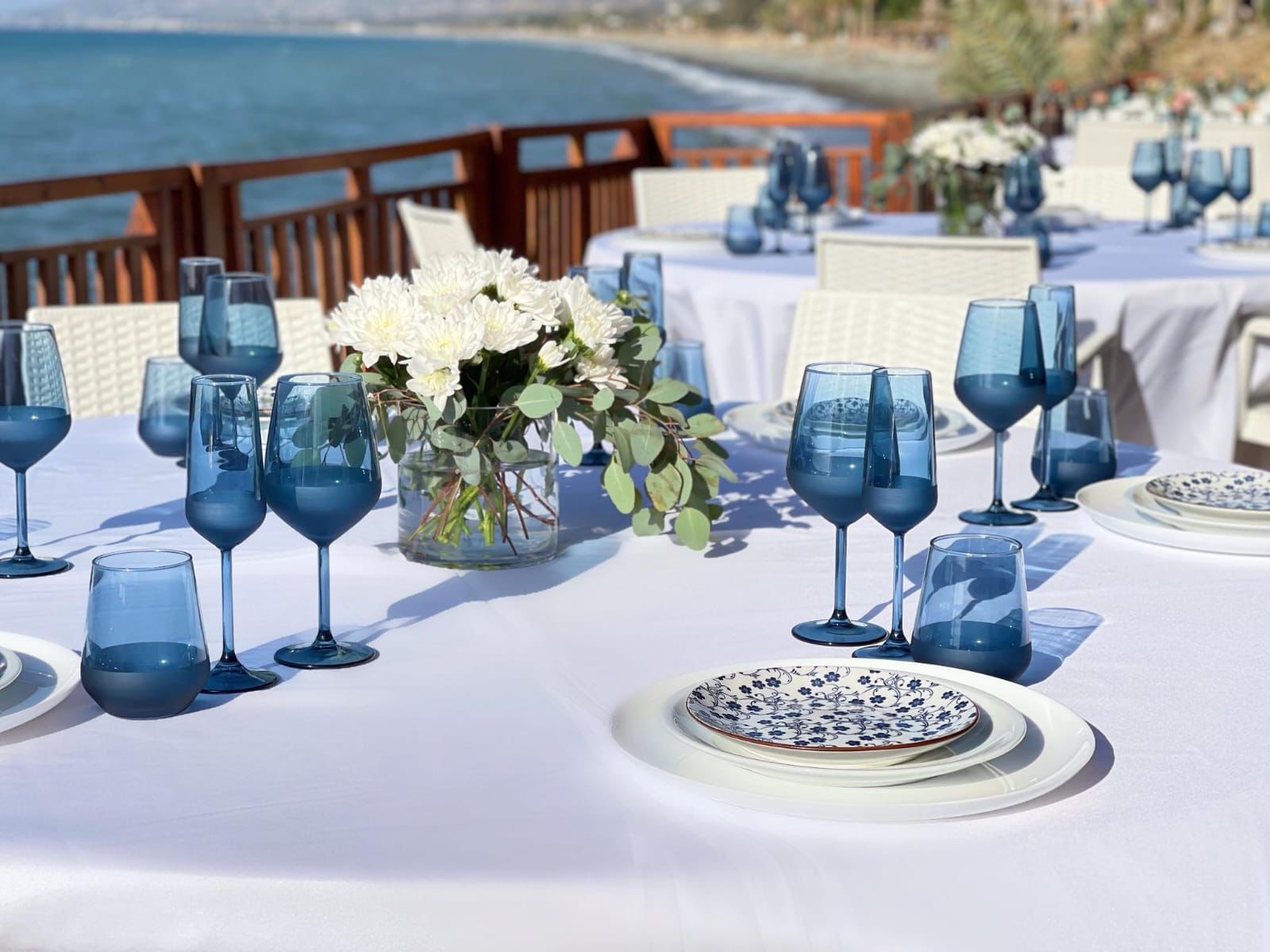 Blue glassware and white flowers on a table beside the sea